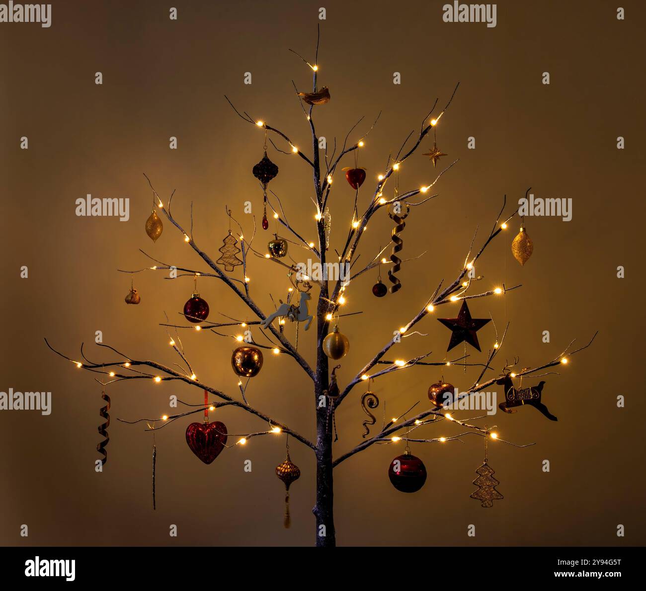 Sapin de Noël moderne de style brindille décoré dans des décorations de Noël traditionnelles rouges et dorées avec effet neige et ligthes sur donnant une lueur chaude Banque D'Images