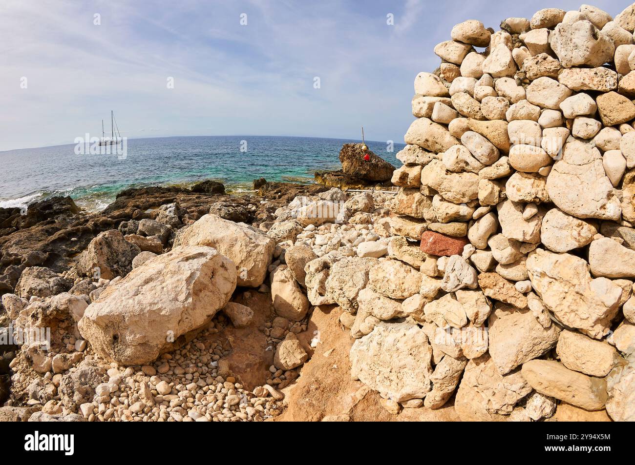 Mur de pierre de cale sèche traditionnelle à la plage de sa Cala avec voilier en arrière-plan (la Mola, Formentera, Îles Baléares, mer Méditerranée, Espagne) Banque D'Images