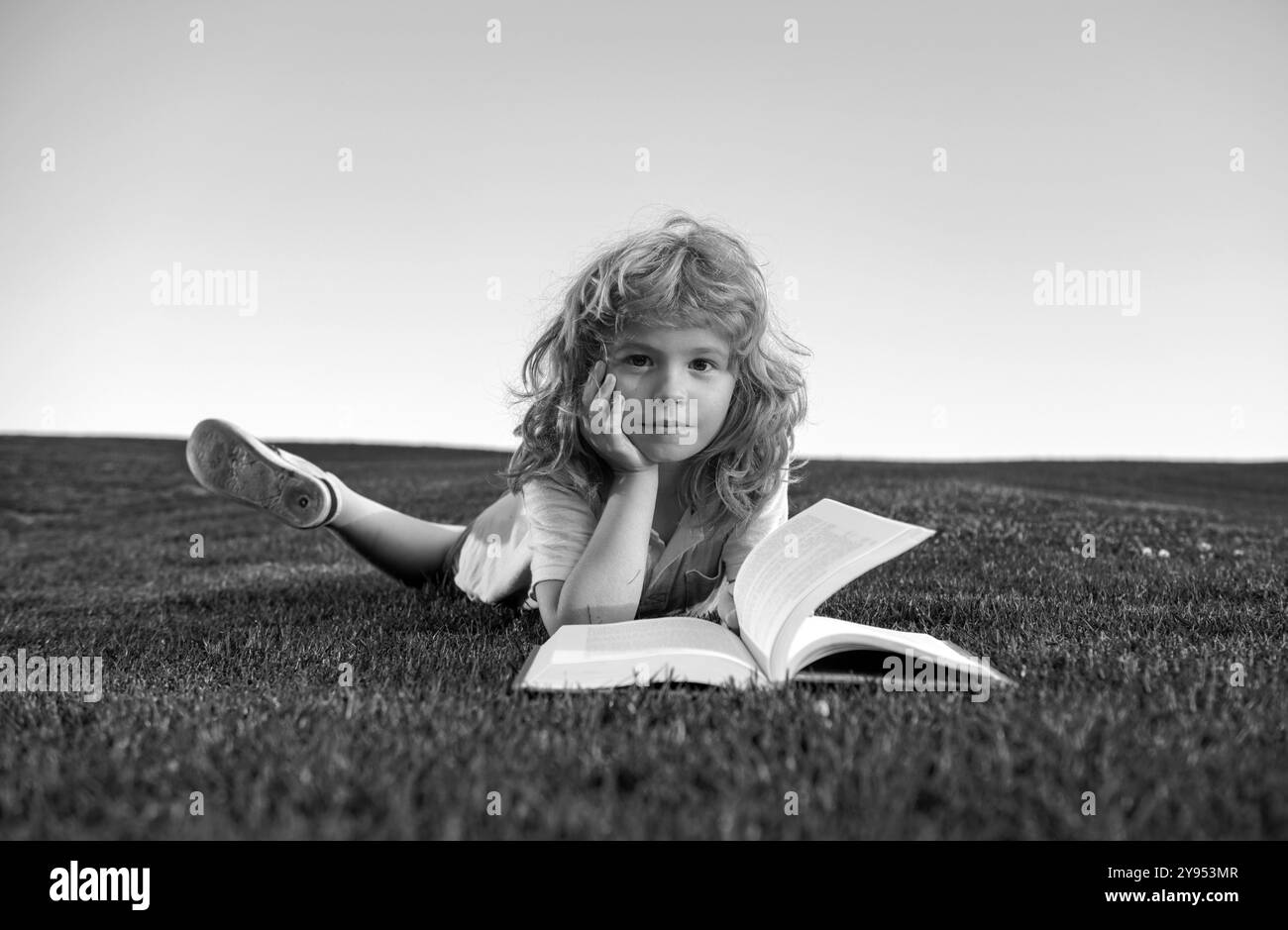 Drôle enfant de lire le livre dans le parc de printemps.Un enfant est en train de lire un livre sur le parc de printemps.Détente sur l'herbe dans le jardin.Éducation en plein air. Banque D'Images