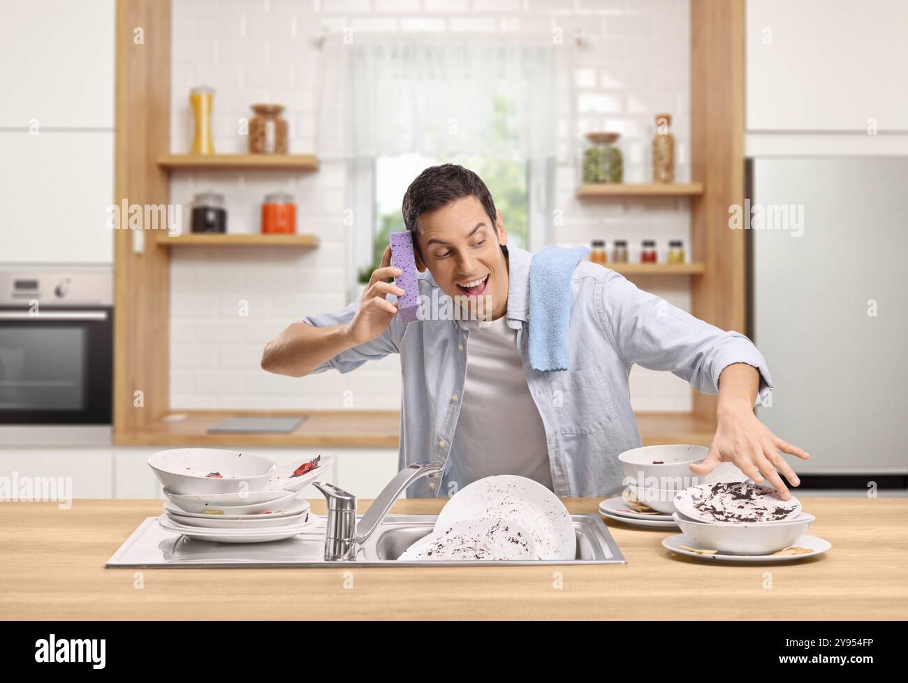 Jeune homme joyeux lavant la vaisselle dans la cuisine et se faisant passer pour un dj Banque D'Images