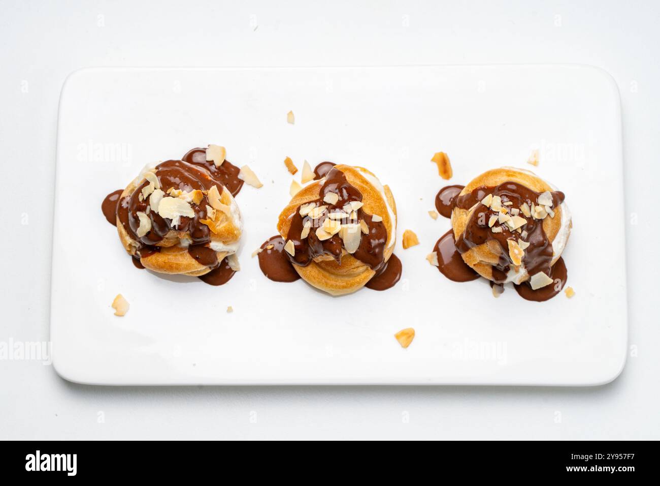 Profiteroles avec crème anglaise, glaçage au chocolat et pétales d'amandes sur une assiette blanche sur un fond clair ou une table. Recette traditionnelle française de dessert. Élevé Banque D'Images