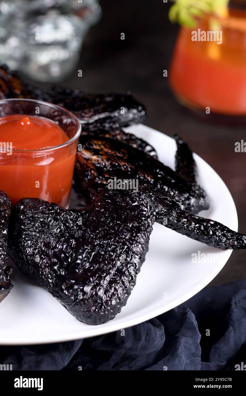 Ailes de chauve-souris. Cuit dans une sauce aigre-douce avec de l'encre de seiche, servi avec du ketchup dans une assiette. Une idée originale pour une fête d'Halloween Banque D'Images