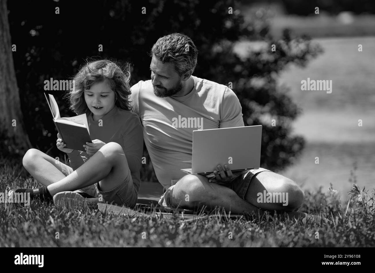 Une famille charmante lisant un livre sur l'herbe. Un garçon et un père pique-nique dans le parc. Un fils heureux et un père lisant un livre. Famille du bonheur. Père lisant un Banque D'Images