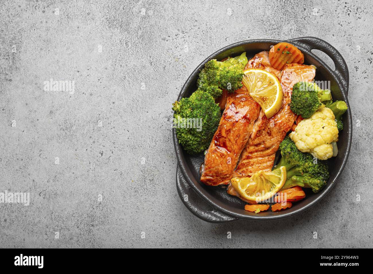 Steaks de saumon de poisson cuit sain, brocoli, chou-fleur, carotte dans un bol de cocotte en fonte noire sur fond de pierre grise. Cuisson d'un délicieux CA faible Banque D'Images