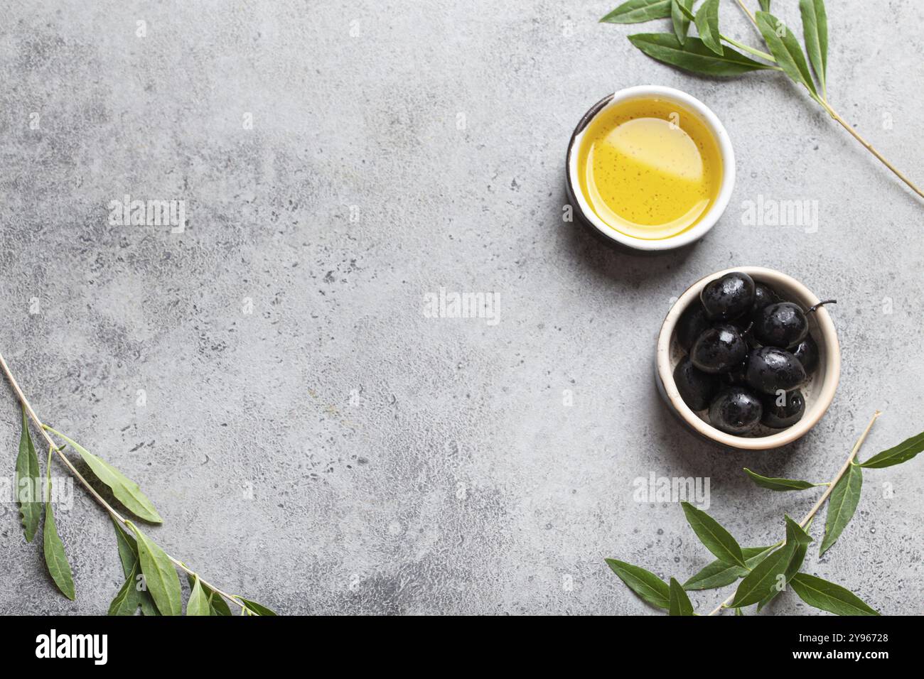 Olives noires et huile d'olive extra vierge dans un petit bol avec des branches d'olivier vue de dessus sur fond de pierre de béton gris, espace pour le texte, photo de nourriture Banque D'Images