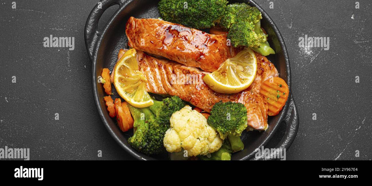 Poisson cuit santé saumon steaks, brocoli, chou-fleur, carotte en fer forgé bol de cocotte fond noir de pierre sombre. Cuisson d'une délicieuse carbe basse Banque D'Images
