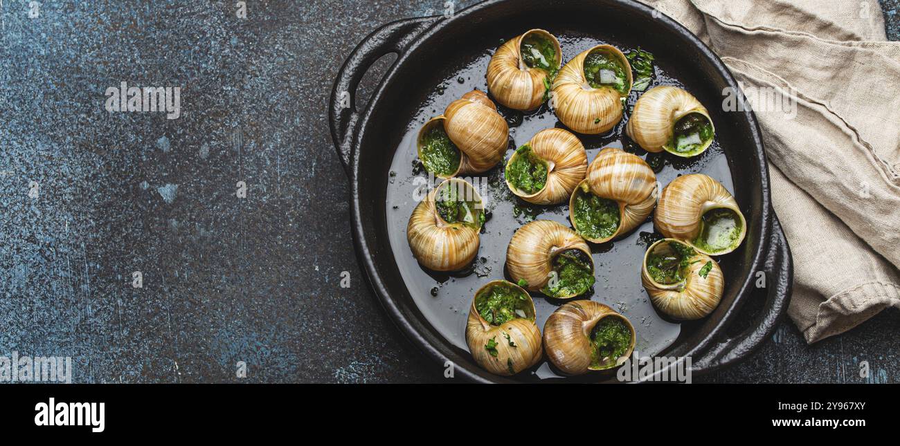 Escargots de Bourgogne escargots avec beurre d'ail et persil dans une poêle en fonte noire sur fond de pierre rustique vue de dessus, délicatesse française traditionnelle, Banque D'Images