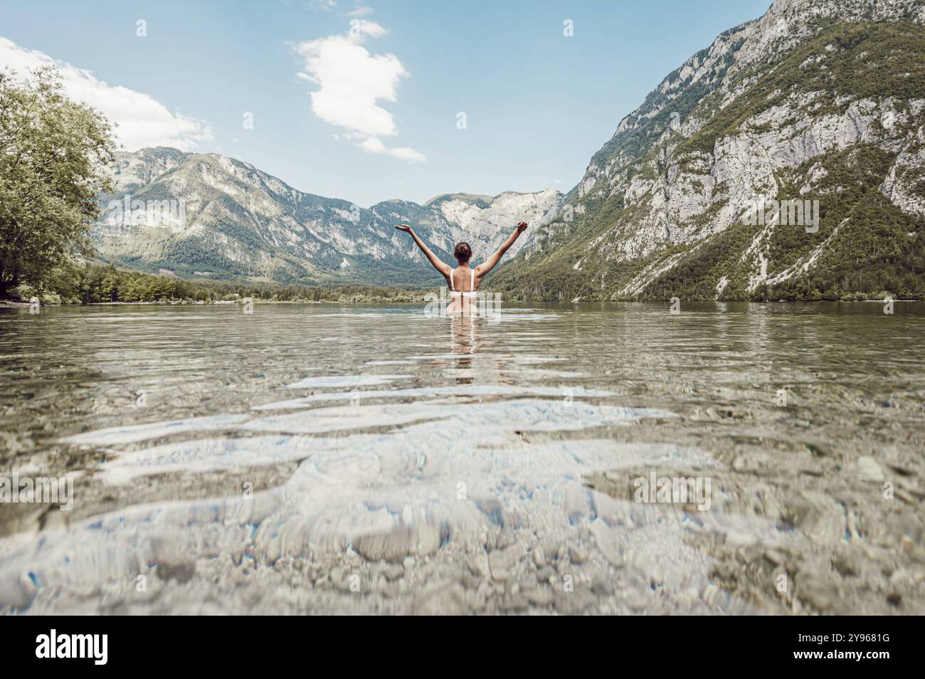 Femme avec les bras tendus vers le ciel des deux côtés dans un lac clair, entouré de montagnes et sous un ciel large, vallée de Soca, Slovénie, Europe Banque D'Images