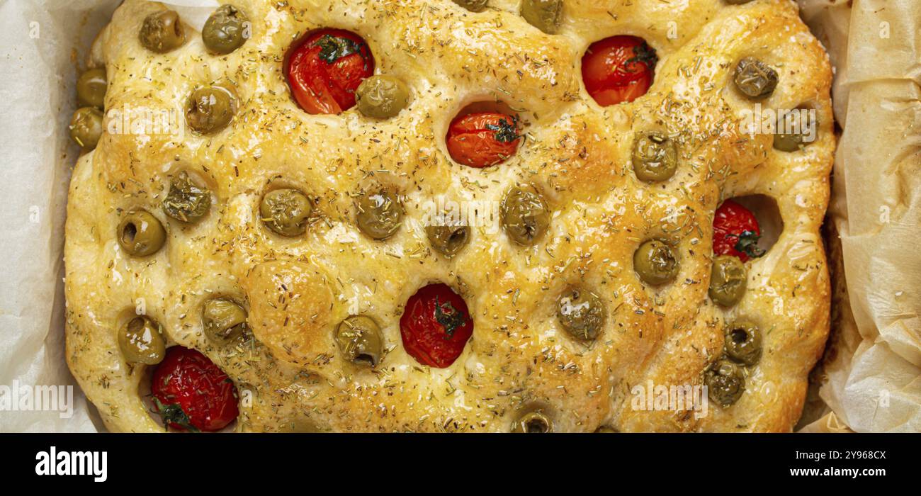 Tête de pain plat traditionnel italien fait maison Focaccia avec olives vertes, huile d'olive, tomates cerises et romarin dans la plaque de cuisson sur rustique sombre Banque D'Images