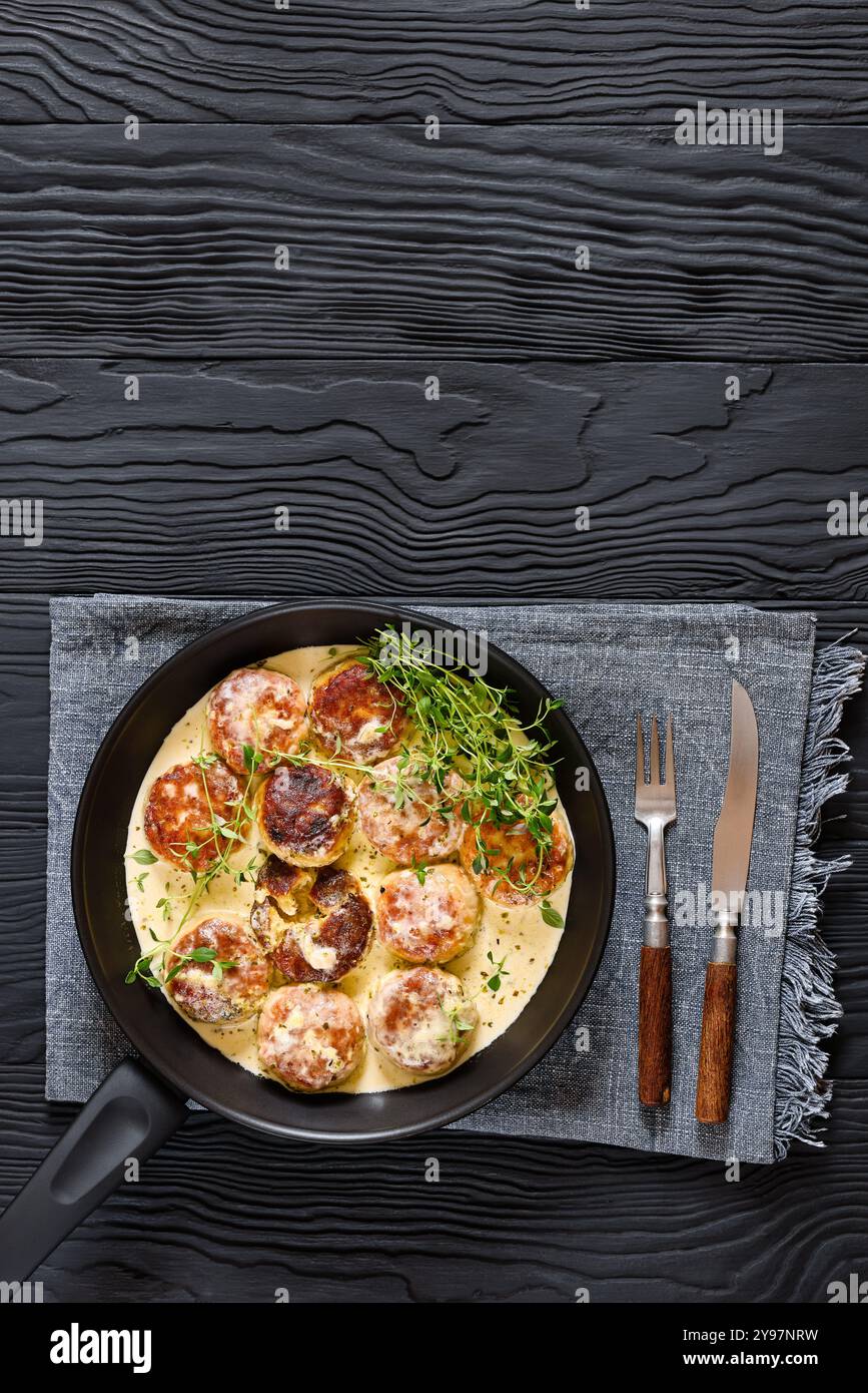 délicieuses rissoles de poulet, galettes dans une sauce à la crème riche avec du thym et assaisonnement sur une poêle sur une table en bois noir avec fourchette et couteau, vue verticale Banque D'Images