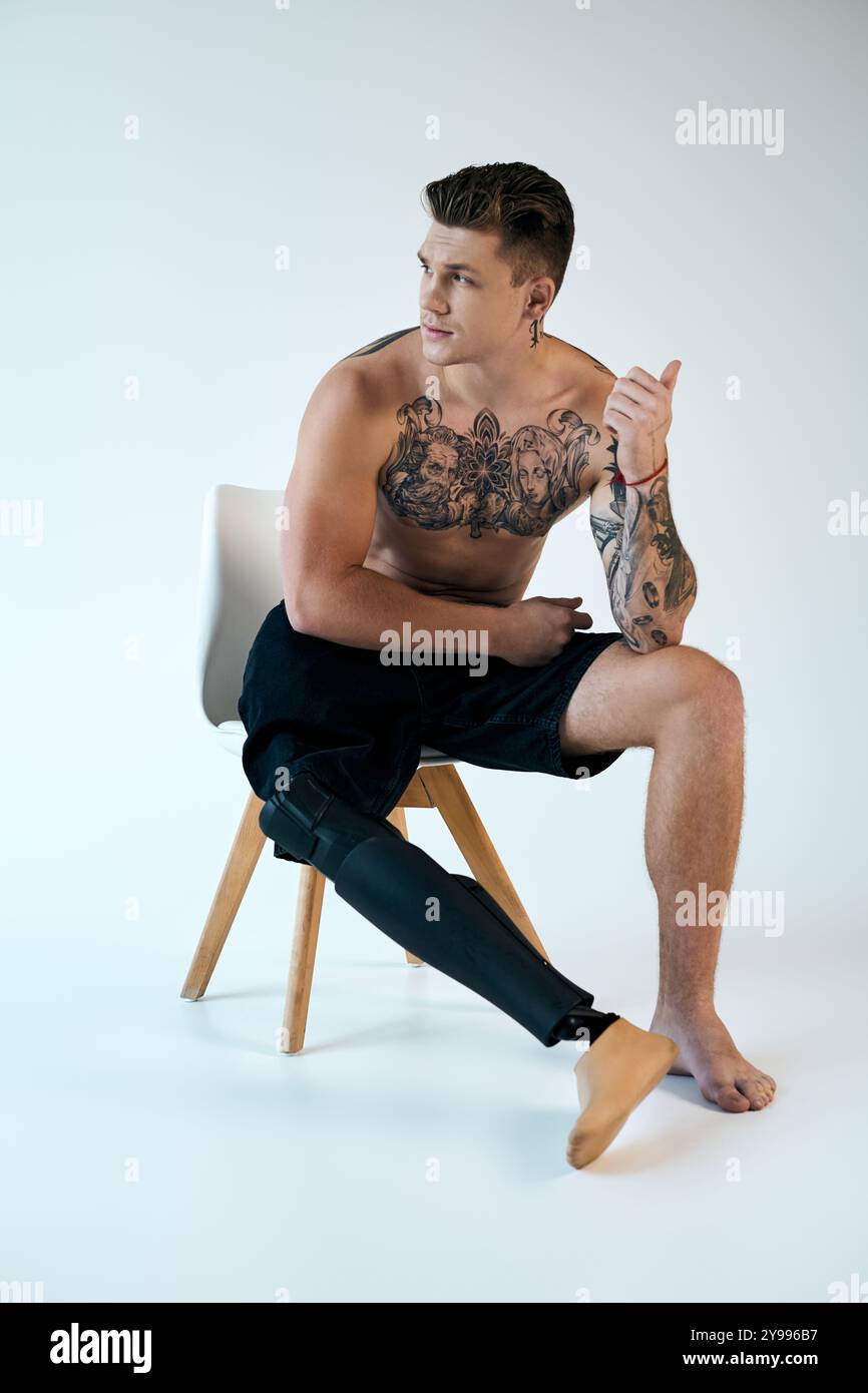 Un jeune homme avec des tatouages est assis sur une chaise, affichant avec confiance sa jambe prothétique dans un studio élégant. Banque D'Images