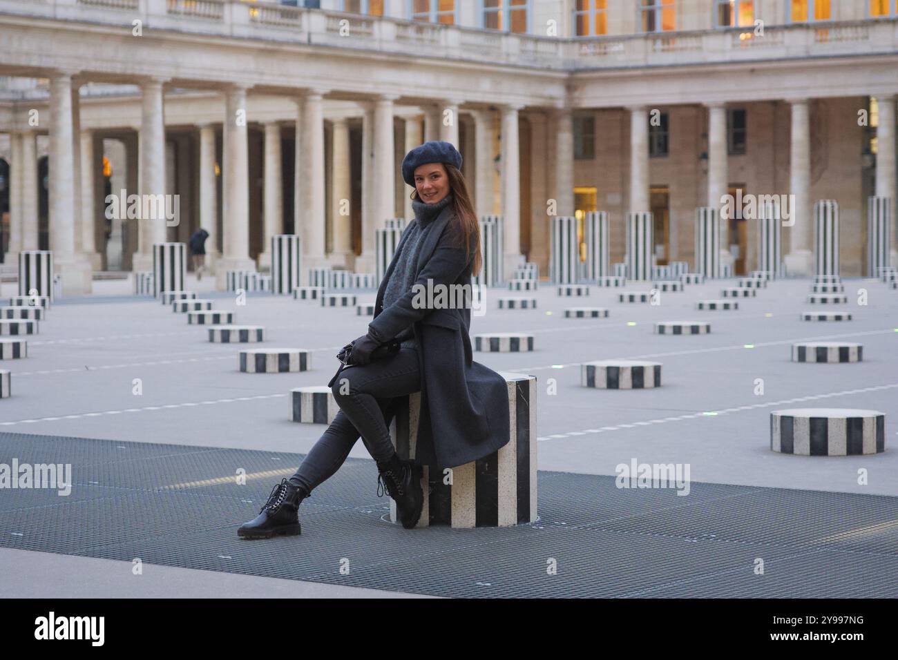 Chic belle femme en manteau d'hiver assis parmi les colonnes de Buren Paris Banque D'Images