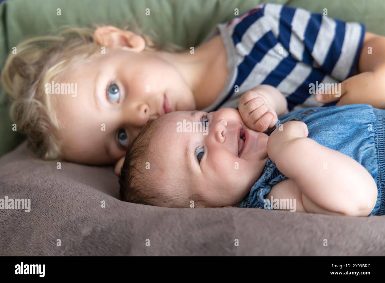 Sa sœur aînée aux longs cheveux blonds se câlin avec sa petite sœur sur un canapé. Mise au point sélective Banque D'Images