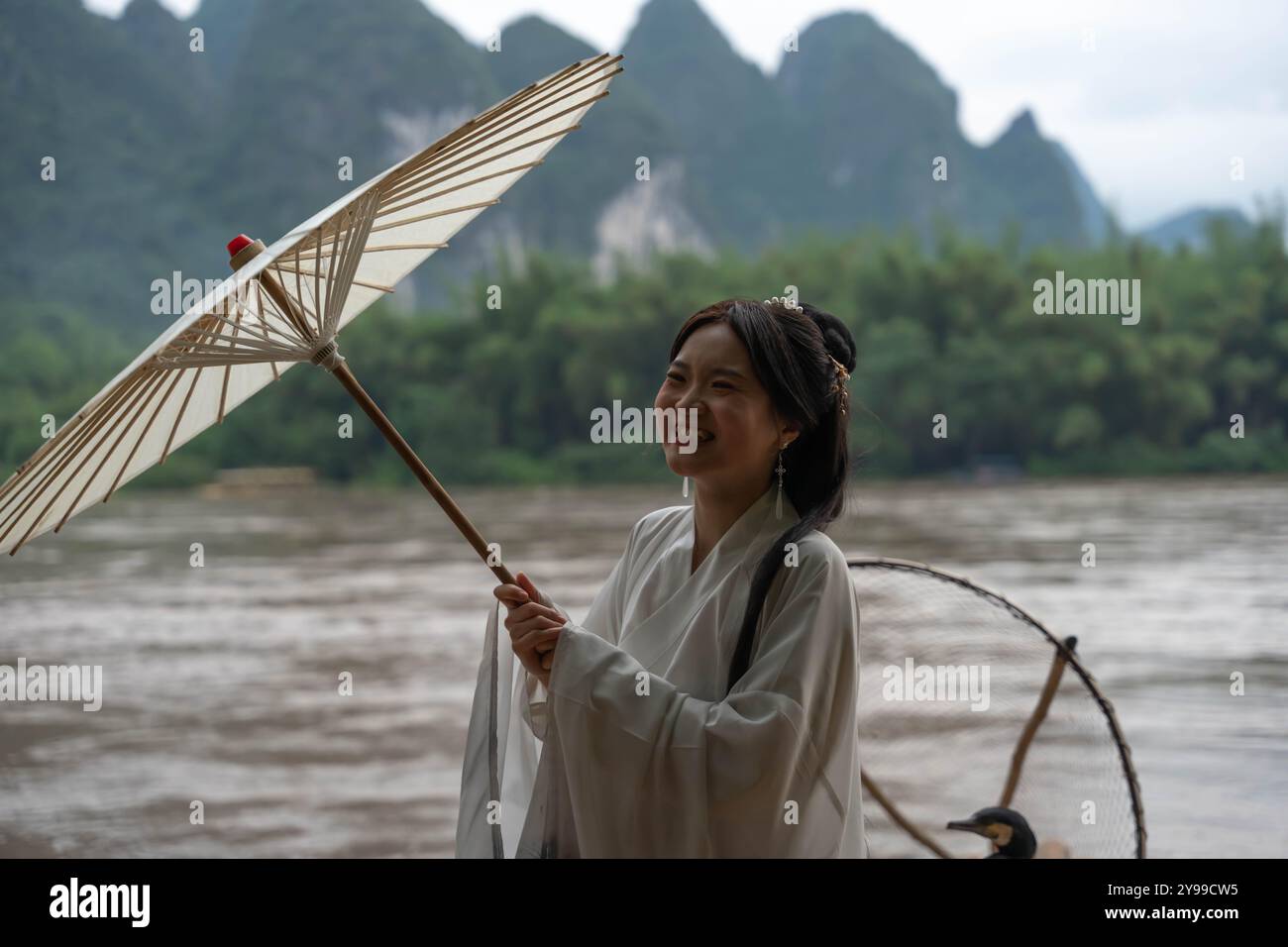 Femme en vêtements Hanfu pouce vers le haut tout en tenant un parapluie sur un radeau de bambou près de Li River à Xingping, Chine Banque D'Images