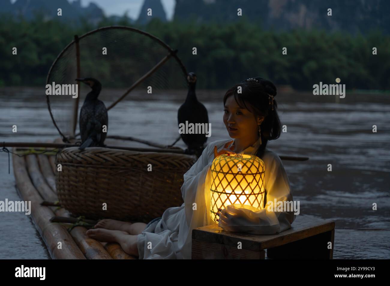 Hanfu fille tenant une lanterne illuminée sur un radeau de bambou avec des oiseaux Cormoran la nuit Banque D'Images