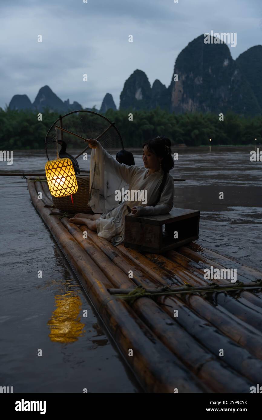 Fille à Hanfu admire un reflet de lanterne d'un radeau de bambou sur la rivière Li à Xingping. Vertical Banque D'Images