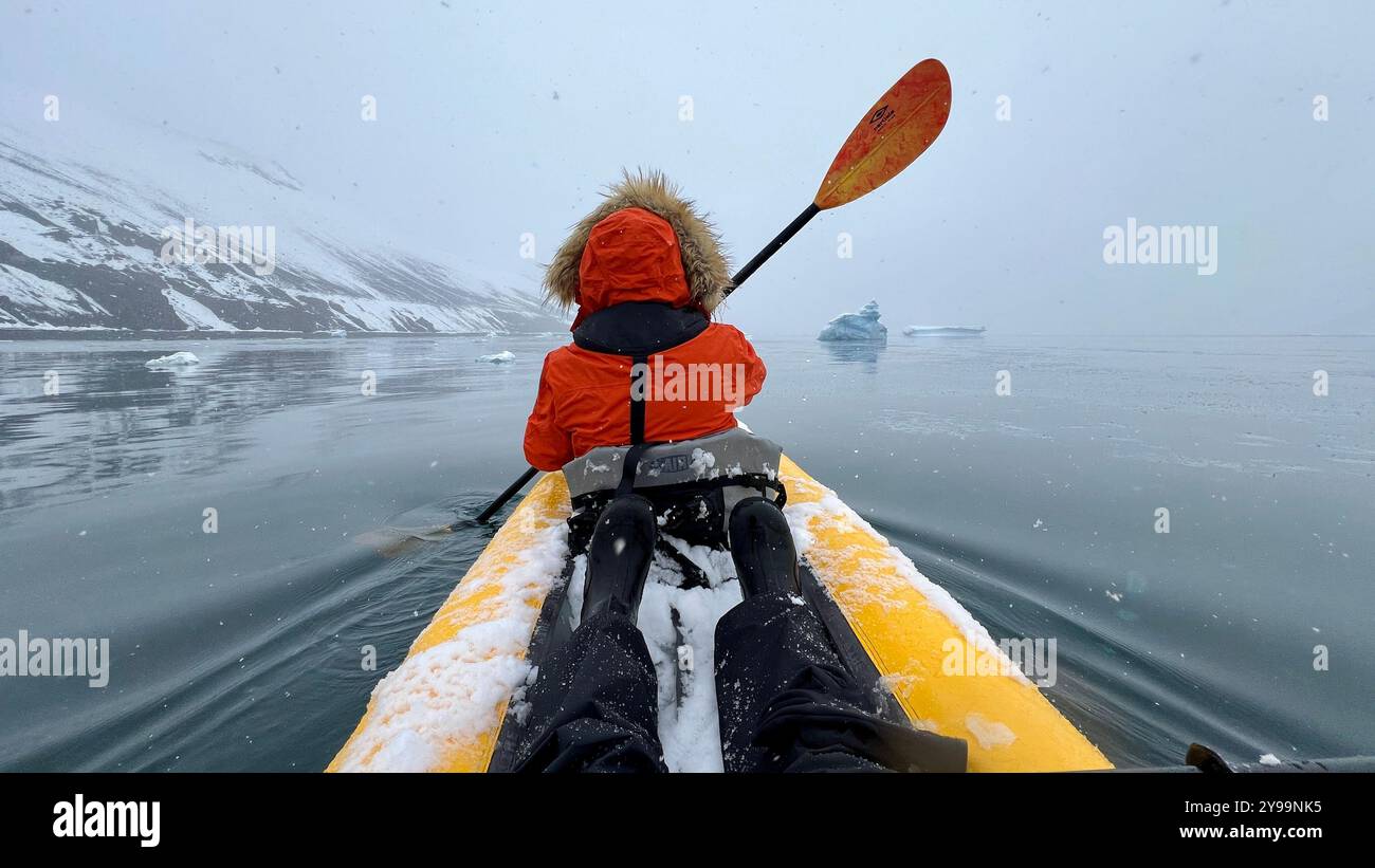Un passager du kayak Nat Geo Endurance traverse des eaux glacées près de la péninsule de Trinity, en Antarctique, avec des montagnes enneigées et des icebergs flottants - Image de stock capturée avec un smartphone