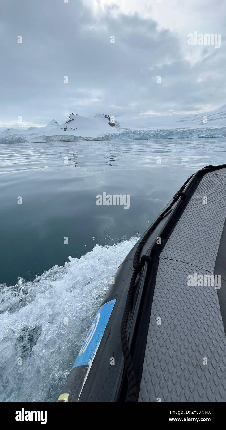 Gros plan d'un bateau d'expédition naviguant dans les eaux calmes de l'Antarctique, avec vue sur les montagnes enneigées et les glaciers au loin - Image de stock capturée avec un smartphone