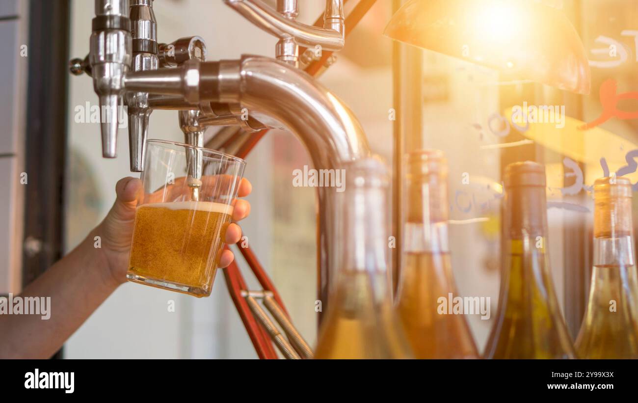 La bière froide est versée dans un verre par le barman du robinet à bière au pub. Image horizontale d'un verre à bière au bar. Banque D'Images