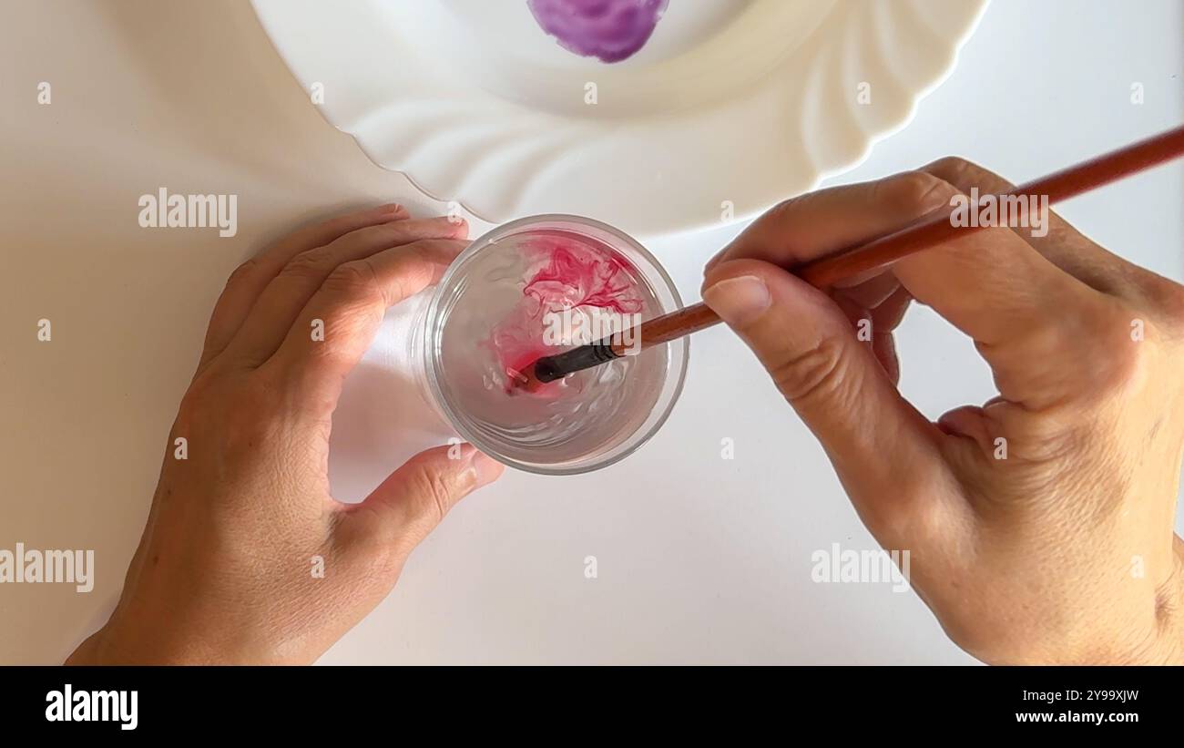 Pinceau tourbillonne l'aquarelle rose dans un verre d'eau clair, vue rapprochée Banque D'Images