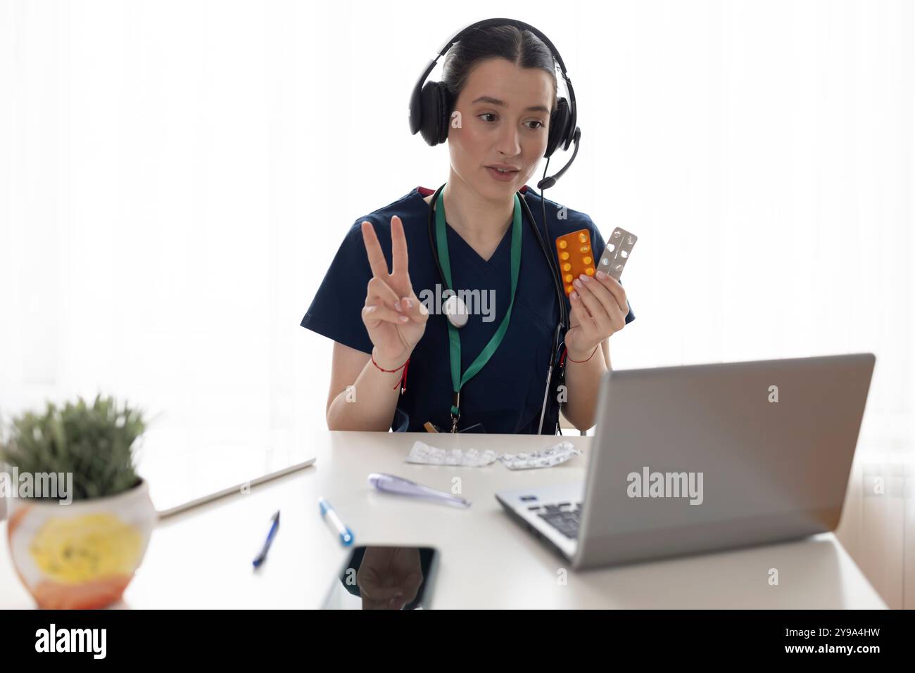 Heureuse belle jeune femme médecin dans des écouteurs parlant au patient sur l'appel vidéo, en utilisant un ordinateur portable pour le chat de conférence en ligne, donnant consul professionnel Banque D'Images