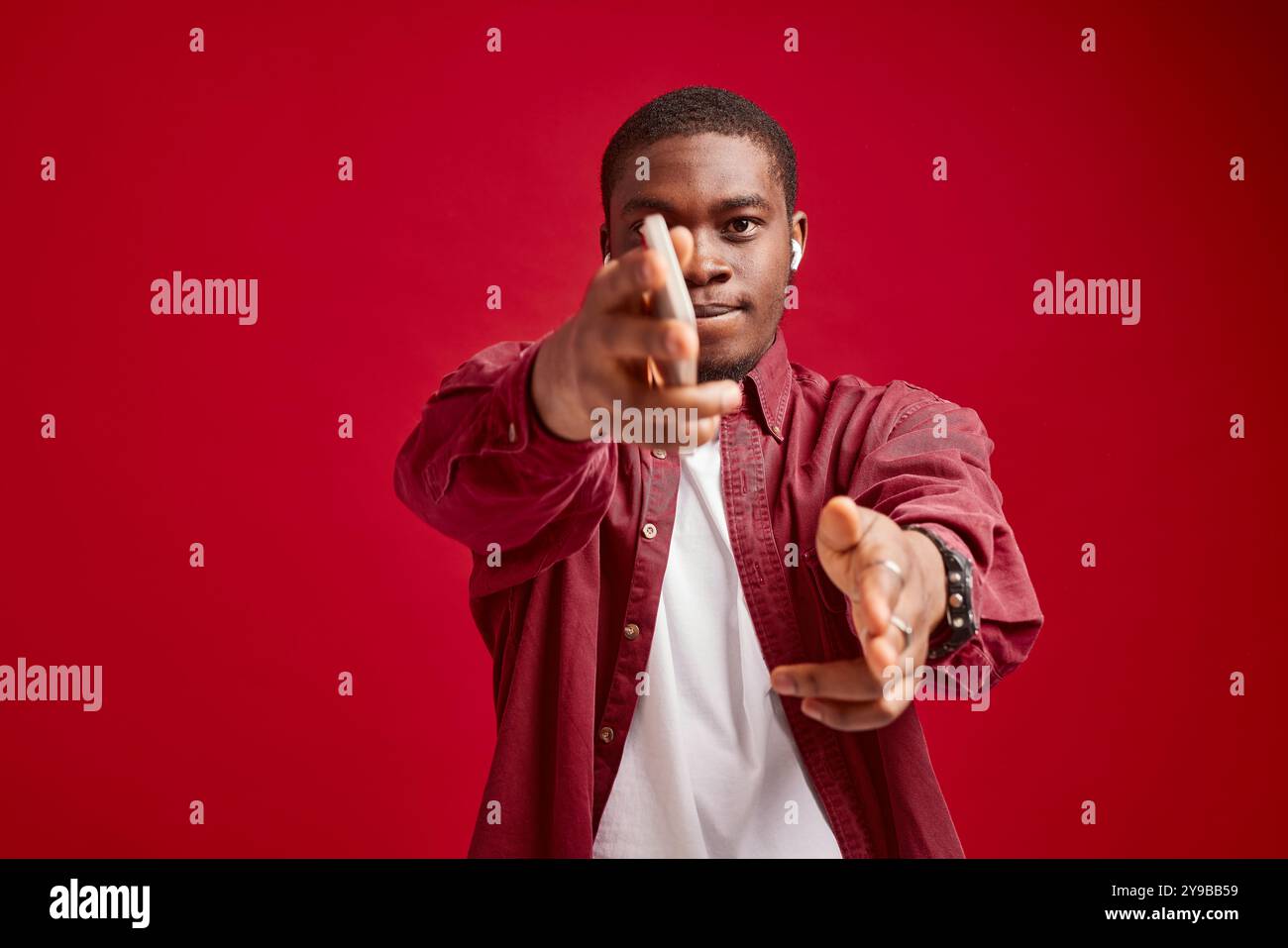 homme émotionnel apparence africaine avec téléphone dans les mains la joie de communication de la technologie, isolé sur fond rouge portrait de studio Banque D'Images