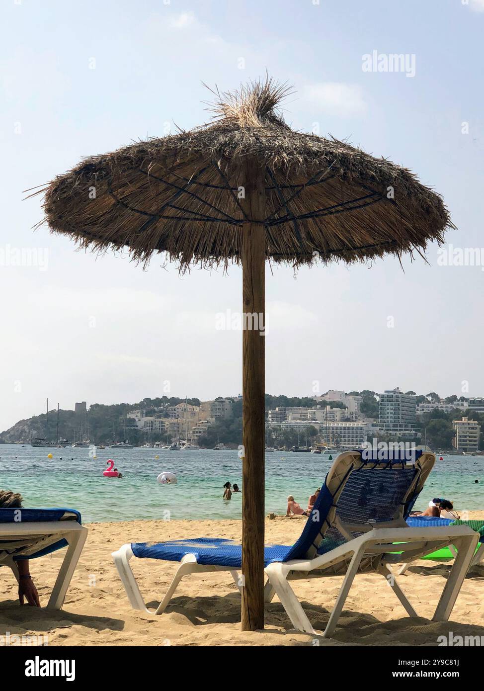 Une scène de plage paisible avec un parasol de paille et des chaises longues face aux eaux chaudes de la plage de Palma Nova sur l'île de Majorque Banque D'Images