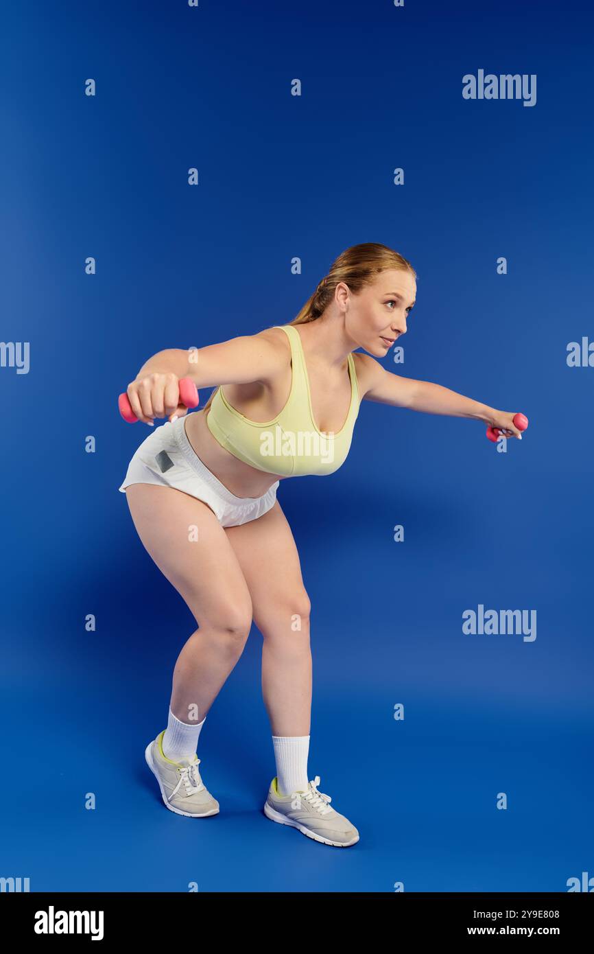 Une sportive dévouée dans un crop top effectue un entraînement en force avec des haltères dans un studio dynamique. Banque D'Images