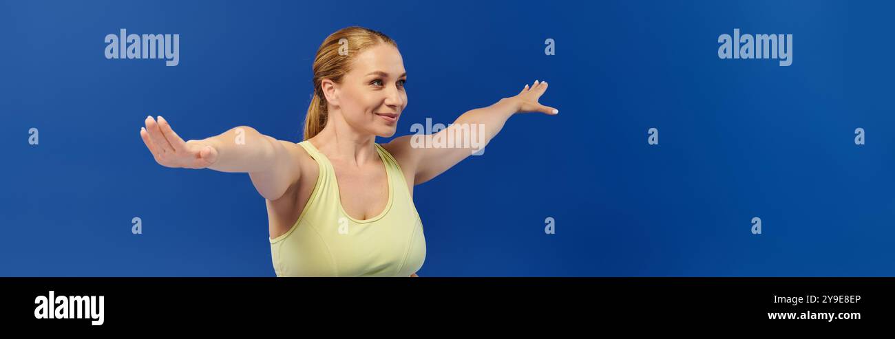 Une femme concentrée dans un crop top effectue un exercice avec les bras étendus, incarnant la forme physique et l'énergie. Banque D'Images