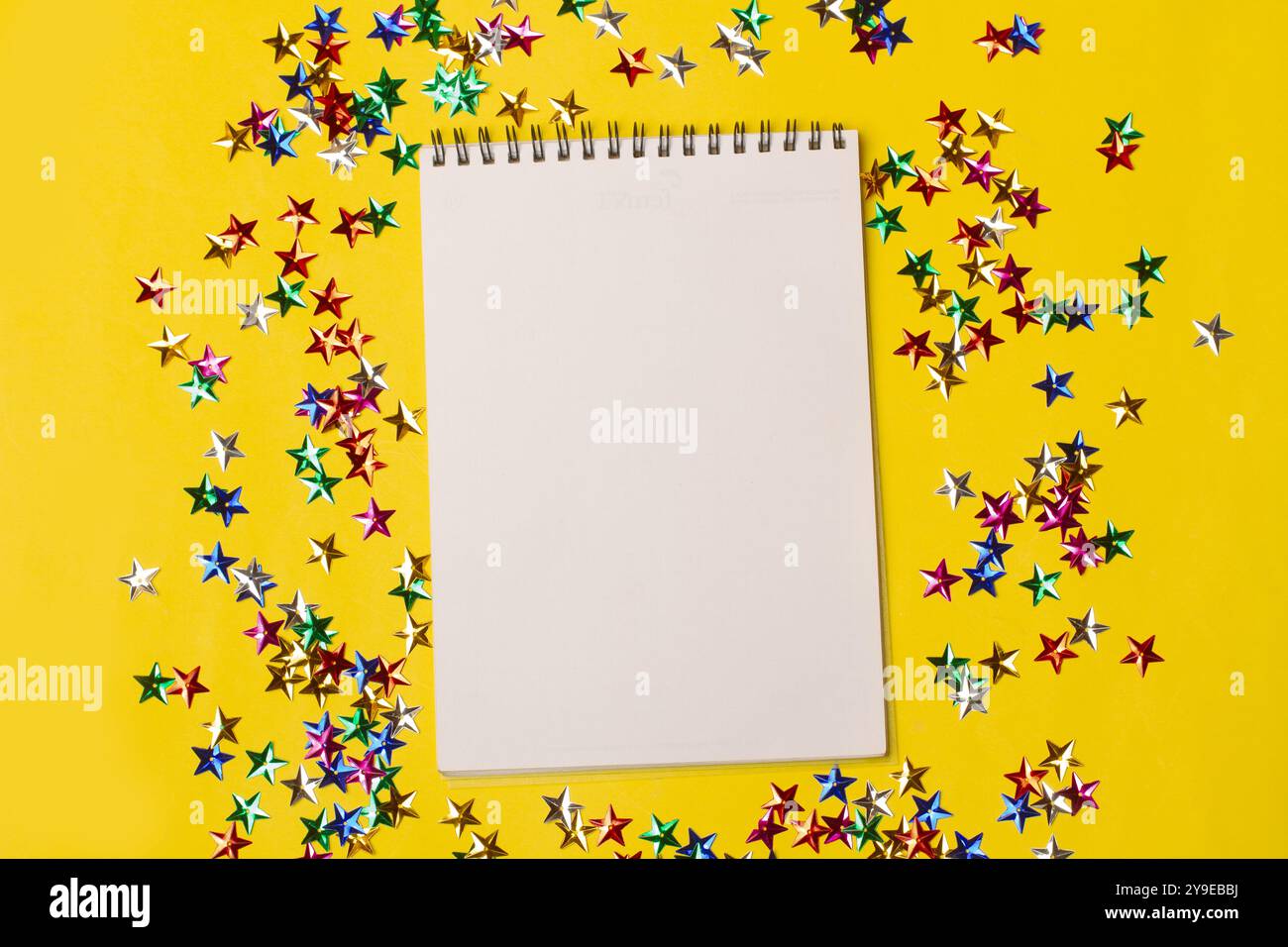 Un carnet ouvert sur une page blanche sur un fond jaune avec des étoiles brillantes de couleur Banque D'Images