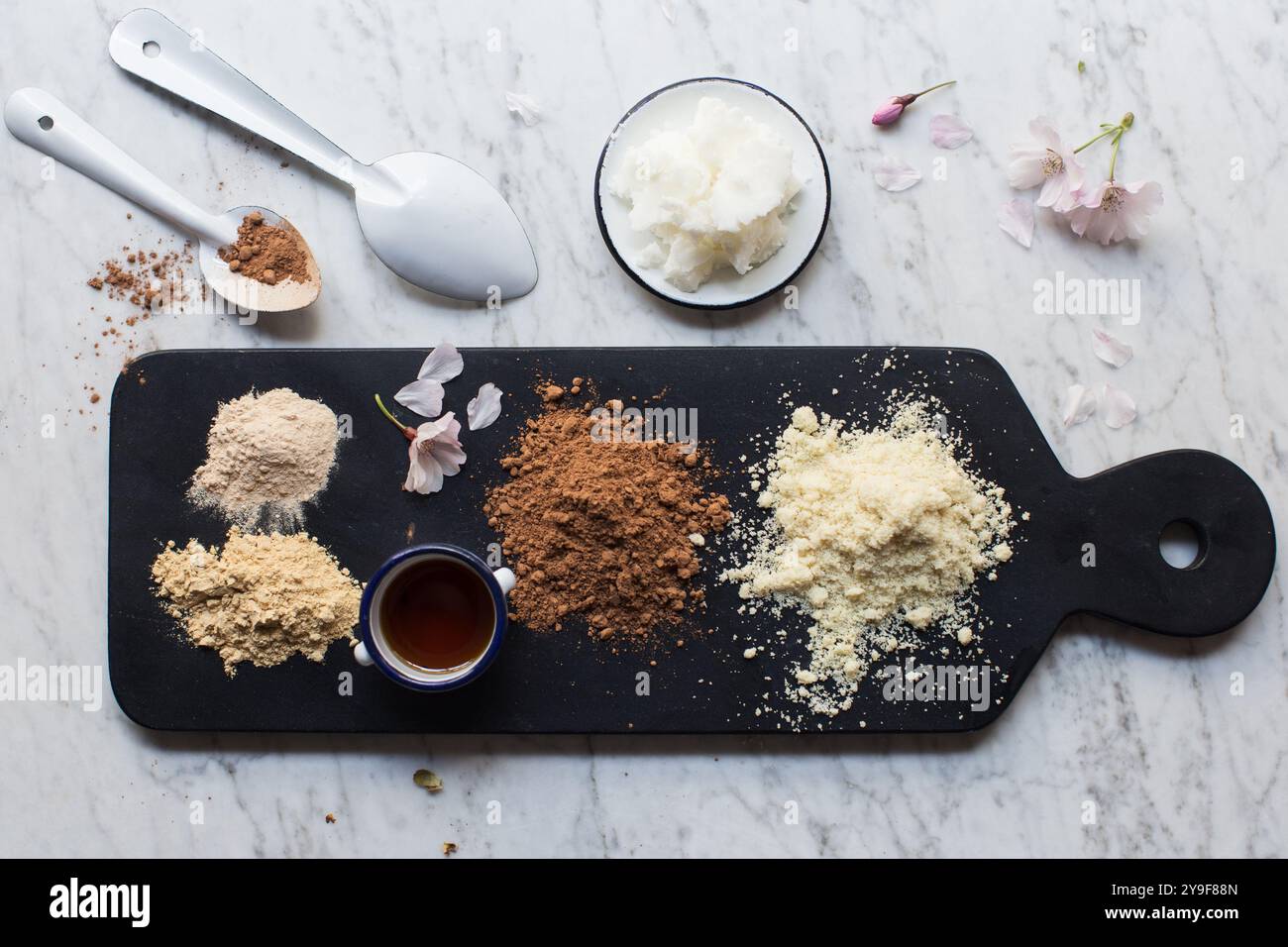 Ingrédients pour chocolat cru fait maison avec poudre de maca. Plat posé sur tableau noir et marbre blanc. Banque D'Images