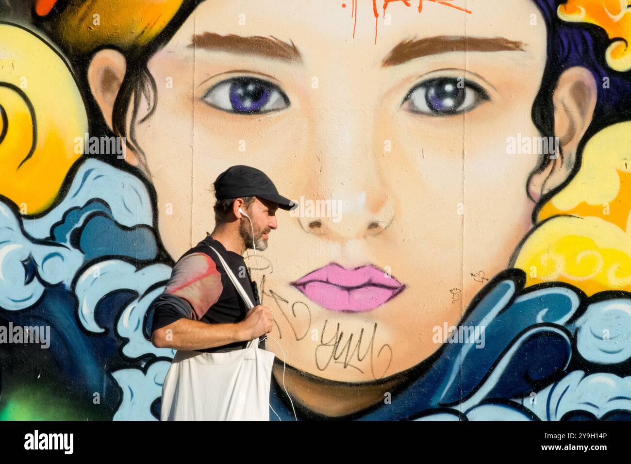 Homme portant des écouteurs écoutant de la musique une personne se promène autour du mur de Street Art Berlin Allemagne Banque D'Images