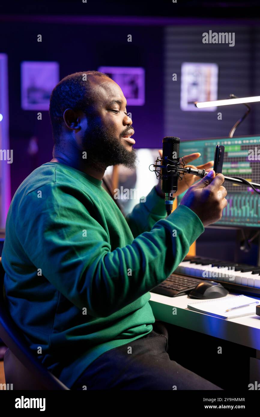 Musicien producteur enregistrant des pistes audio sur microphone pour faire du mix et du master en post-production. Artiste interprétant une version acoustique de sa nouvelle chanson, utilise du matériel stéréo dans le home studio. Banque D'Images