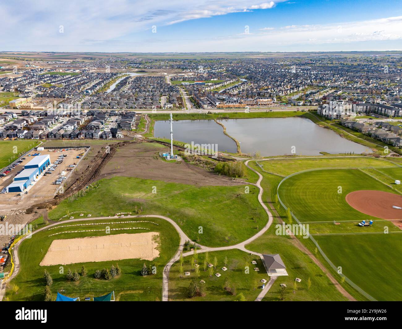 Airdrie Alberta Canada, mai 25 2024 : vue aérienne vers le bas d'un étang lointain de rétention d'égouts pluviaux le long d'un parc public avec de grands chemins et des surplombs Banque D'Images