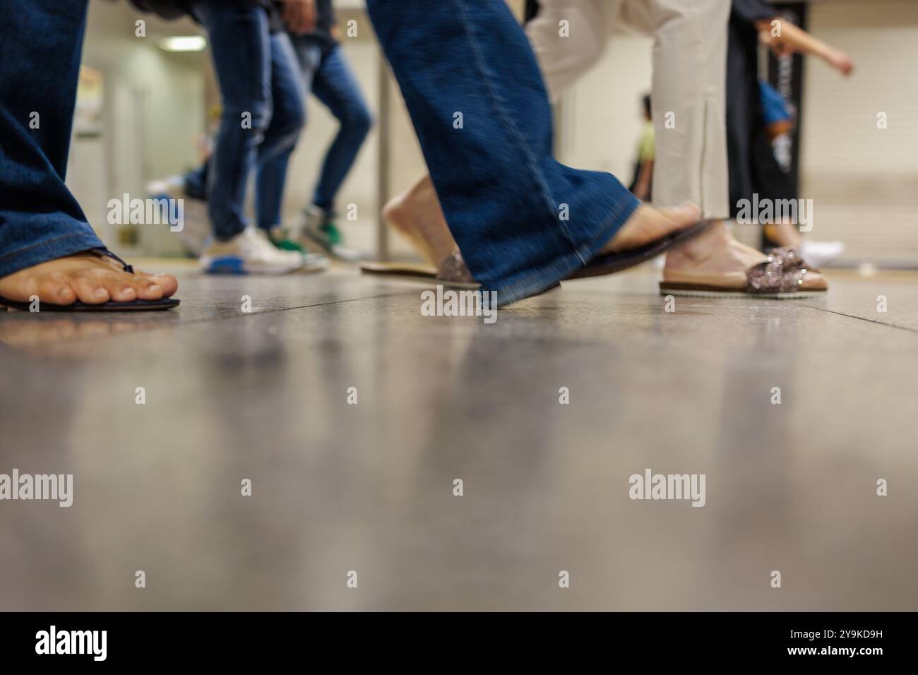 Plusieurs paires de jambes et de pieds se déplacent sur un sol poli dans ce qui semble être un lieu public. L'accent est mis sur les jambes et les chaussures, avec un peu Banque D'Images