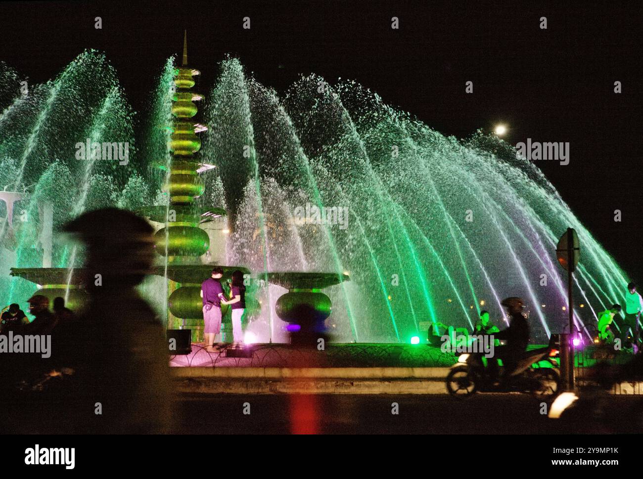 Les gens s'amusent à une fontaine, en premier plan de la circulation routière en soirée à Palembang, Sumatra Sud, Indonésie. Banque D'Images