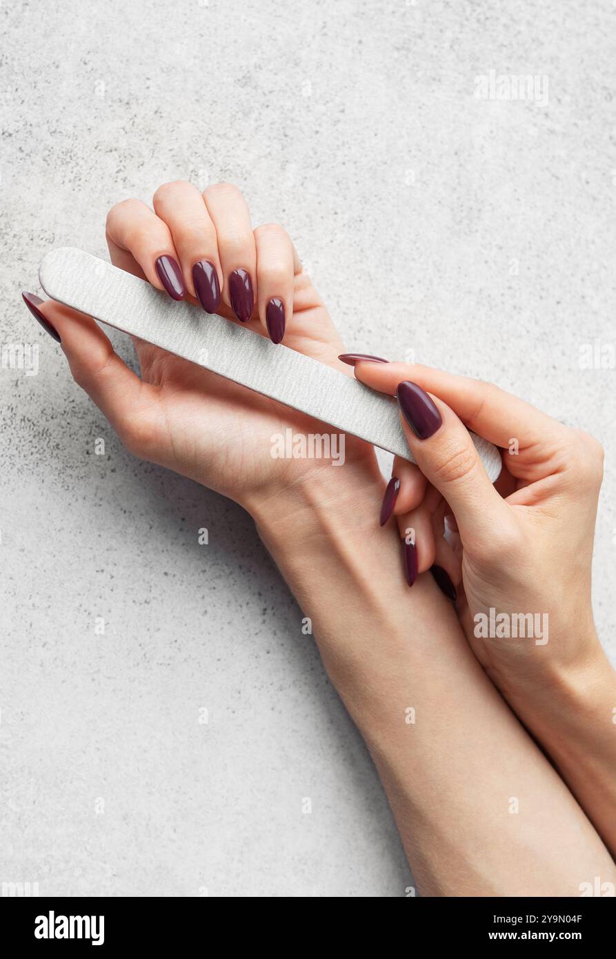 Une personne remplit soigneusement ses ongles à la maison, en utilisant une lime à ongles pour façonner et lisser les bords, créant un look élégant pour une manucure. Banque D'Images