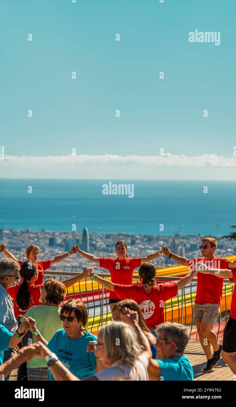 Groupe de personnes dansant la danse folklorique catalane, la sardane avec vue sur la ville de Barcelone et sa mer sous un ciel bleu clair et ensoleillé. Banque D'Images