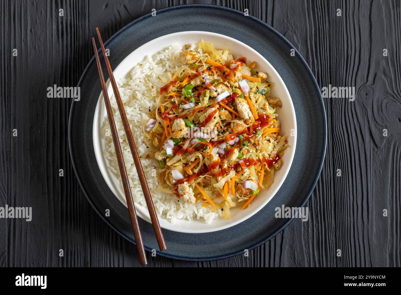 roulé aux œufs de tofu végétalien, chou sauté, tofu émietté assaisonné servi dans une sauce sucrée et salée servi sur du riz dans un bol avec des baguettes sur woo noir Banque D'Images