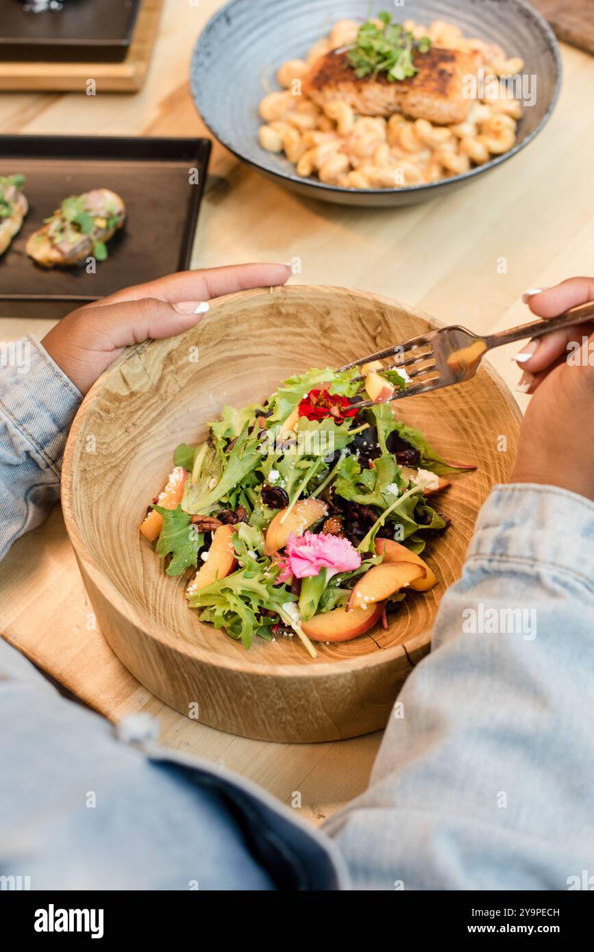 Femme mangeant un bol de salade avec de la nourriture en arrière-plan Banque D'Images