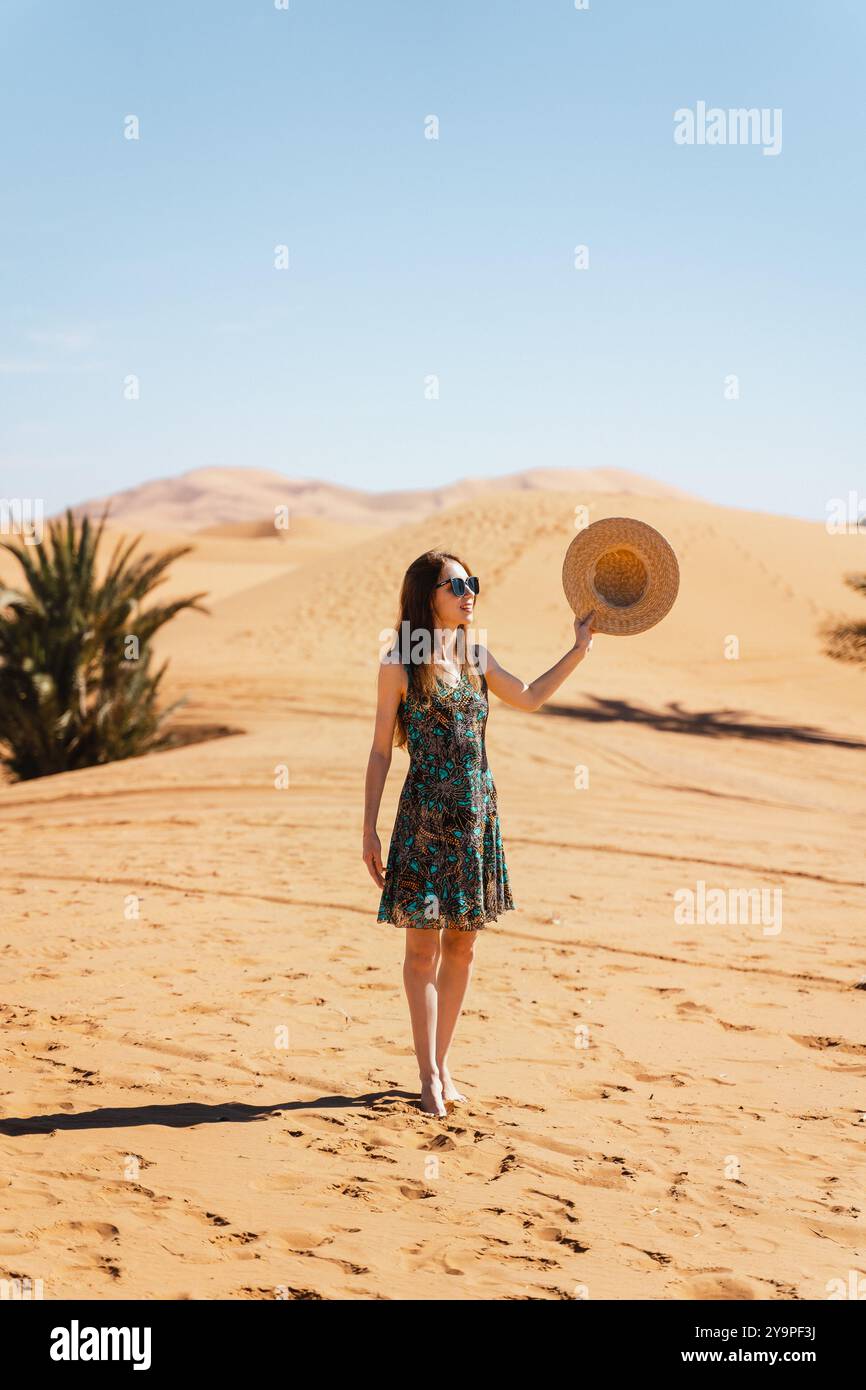Une femme avec un chapeau dans les mains se tient dans le désert du Sahara Banque D'Images