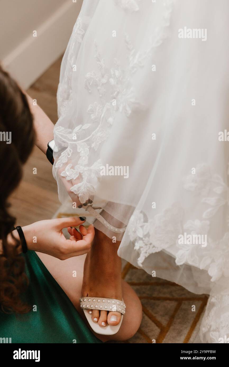 Demoiselle d'honneur attachant la chaussure ornée de perles de la mariée Banque D'Images