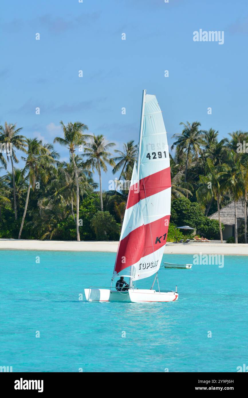 Randheli, Maldives - 24 février 2012 : un instructeur de voile maldivien sur un catamaran Hobie Cat avec une station balnéaire et un hors-bord en arrière-plan Banque D'Images