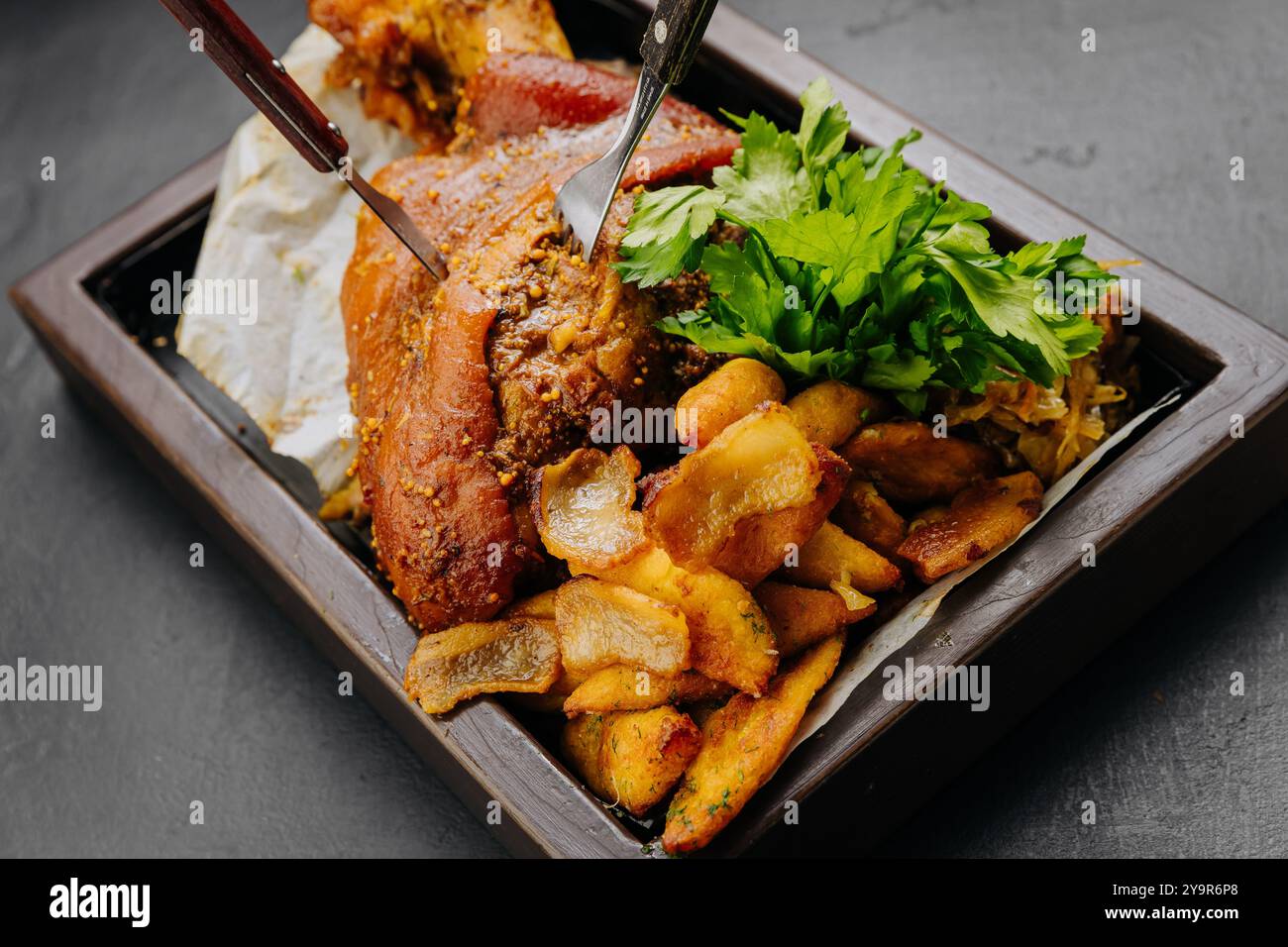 Jarret de porc rôti avec pommes de terre et herbes fraîches sur un plateau en bois, photographie de stock de nourriture Banque D'Images Jarret de porc rôti avec pommes de terre et herbes fraîches sur un plateau en bois, photographie de stock de nourriture Banque D'Images