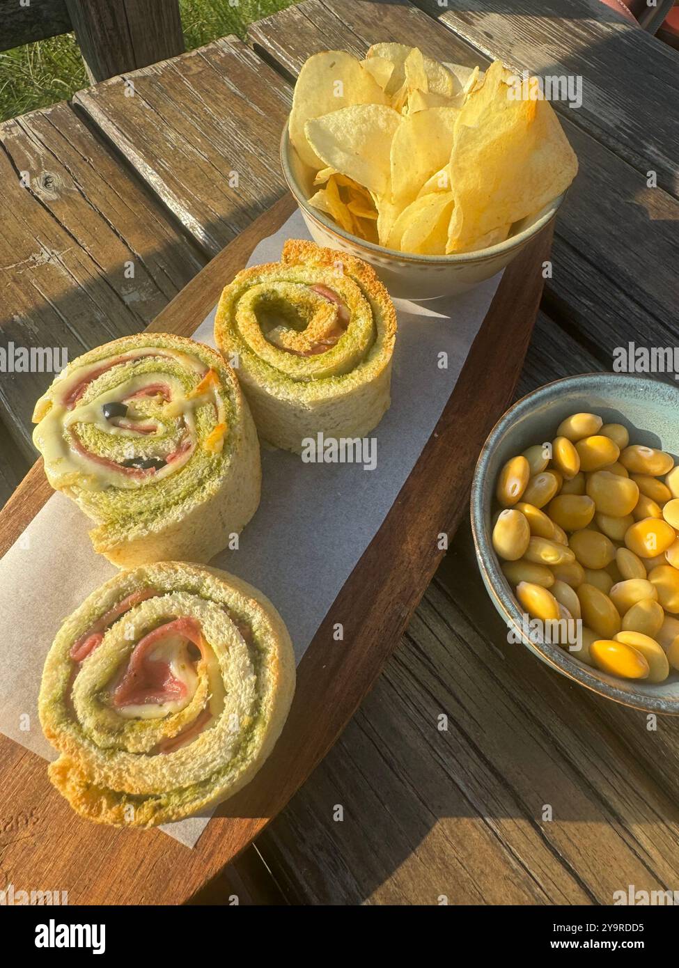 Roulés gourmands pour sandwichs au jambon et au fromage servis avec des chips de pommes de terre et des olives vertes sur une planche de bois, île de São Miguel, Açores. Banque D'Images