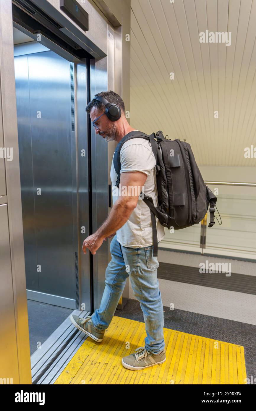 Homme d'âge moyen en vêtements décontractés avec sac à dos entrant dans l'ascenseur à la gare pour accéder aux plates-formes Banque D'Images