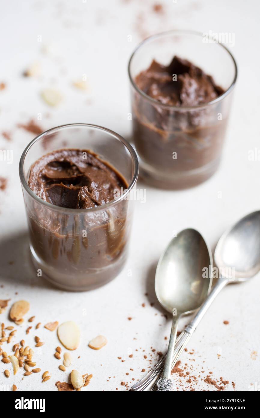 Mousse au chocolat à l'avocat dans des pots en verre avec du cacao et des noix, dessert crémeux sans produits laitiers, indulgence saine sur fond clair. Banque D'Images