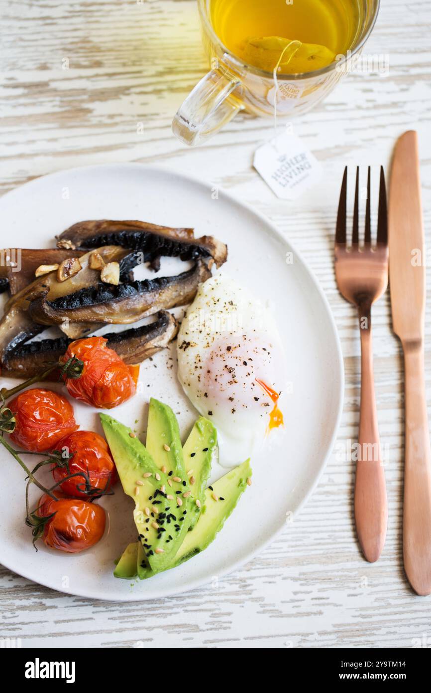 Petit déjeuner sain avec oeuf poché coulant, avocat, tomates cerises rôties et champignons sautés à l'ail. Banque D'Images