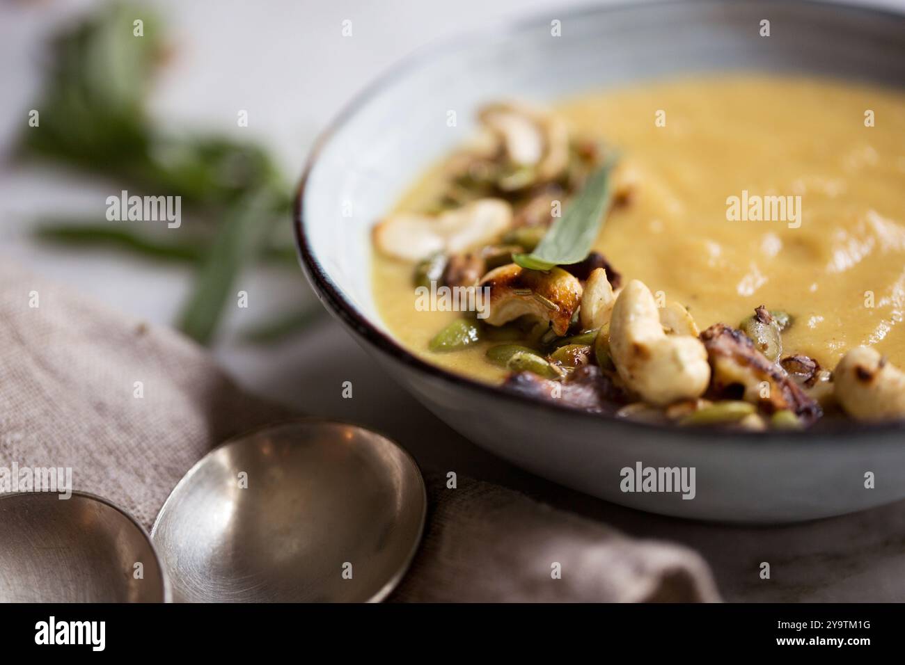 Soupe de chou-fleur rôtie servie dans un bol en céramique grise garni de noix de cajou grillées et de graines de citrouille. Banque D'Images Soupe de chou-fleur rôtie servie dans un bol en céramique grise garni de noix de cajou grillées et de graines de citrouille. Banque D'Images