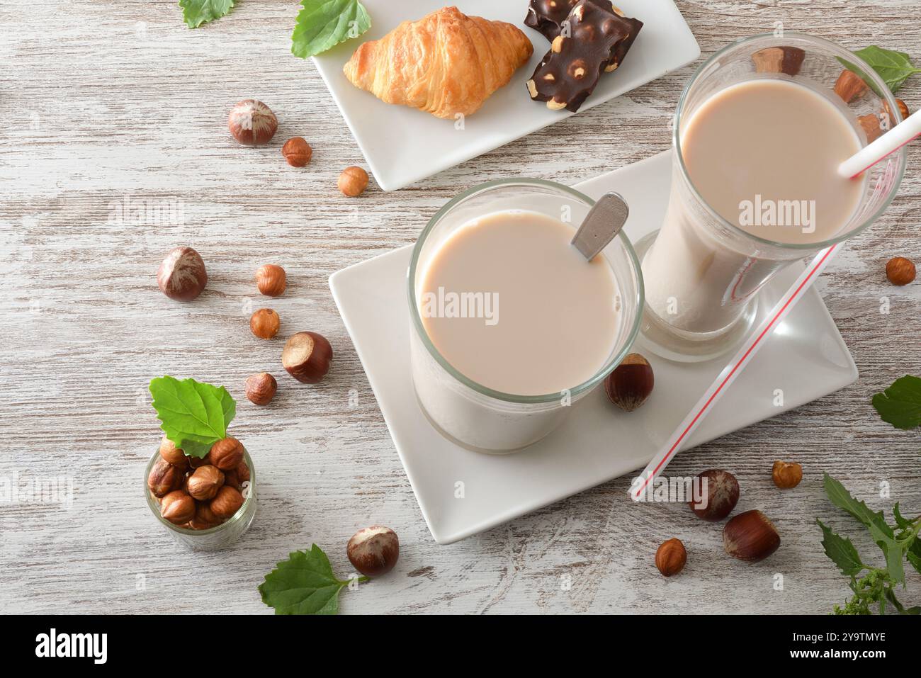 Petit déjeuner préparé sur une table en bois avec deux verres en cristal avec une boisson rafraîchissante aux noisettes et une petite assiette avec du chocolat et un croissant décoré Banque D'Images